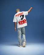 Person wearing a t-shirt with a graphic and text on the back, standing against a blue background